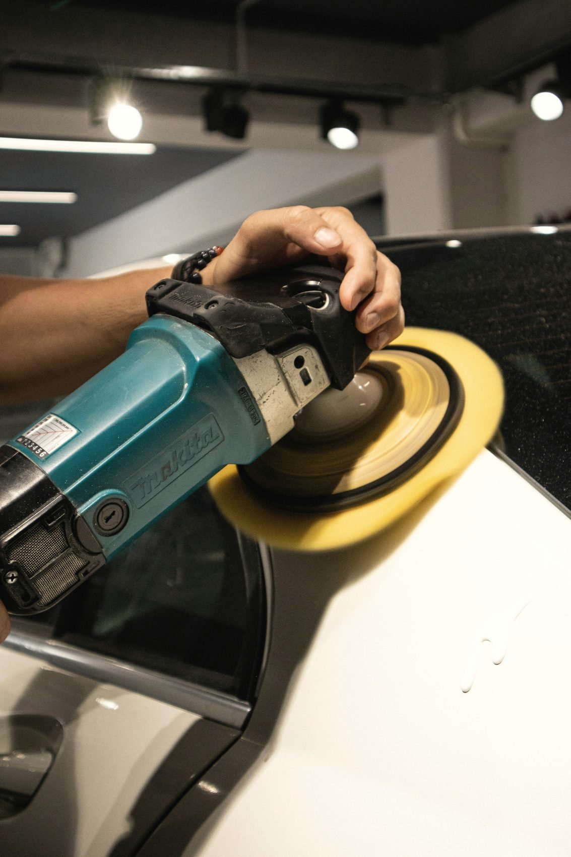 A hand guiding a machine polisher across a white car panel