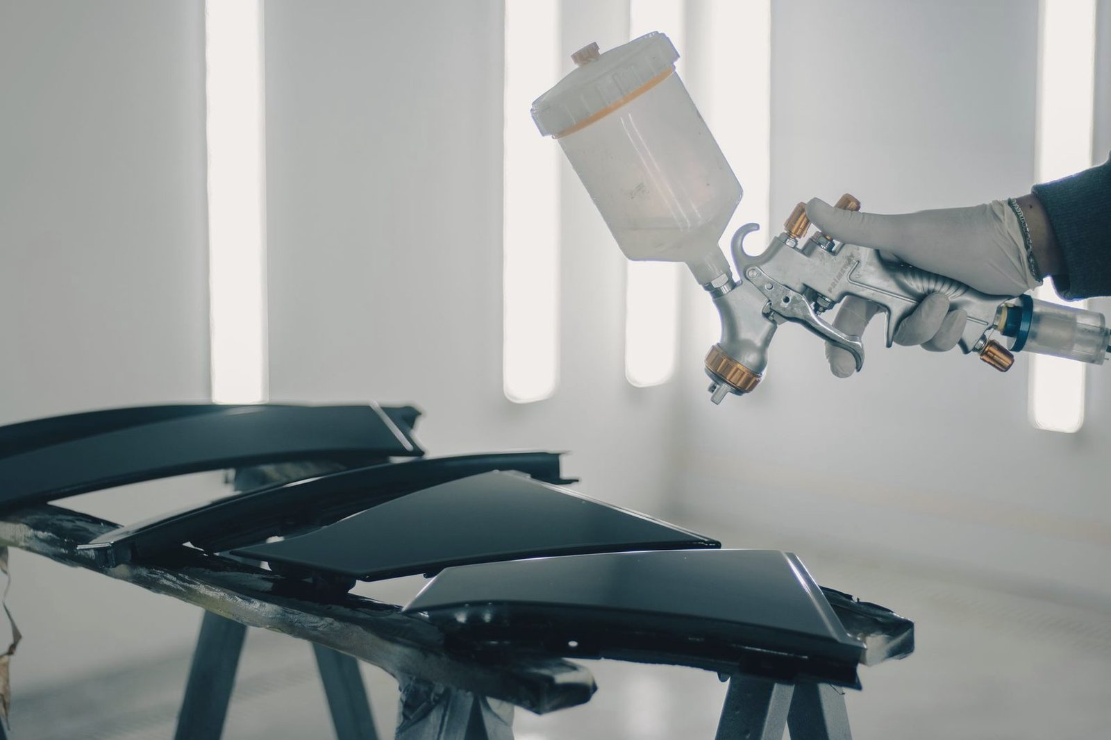 A spray gun held above dark painted panels resting on stands